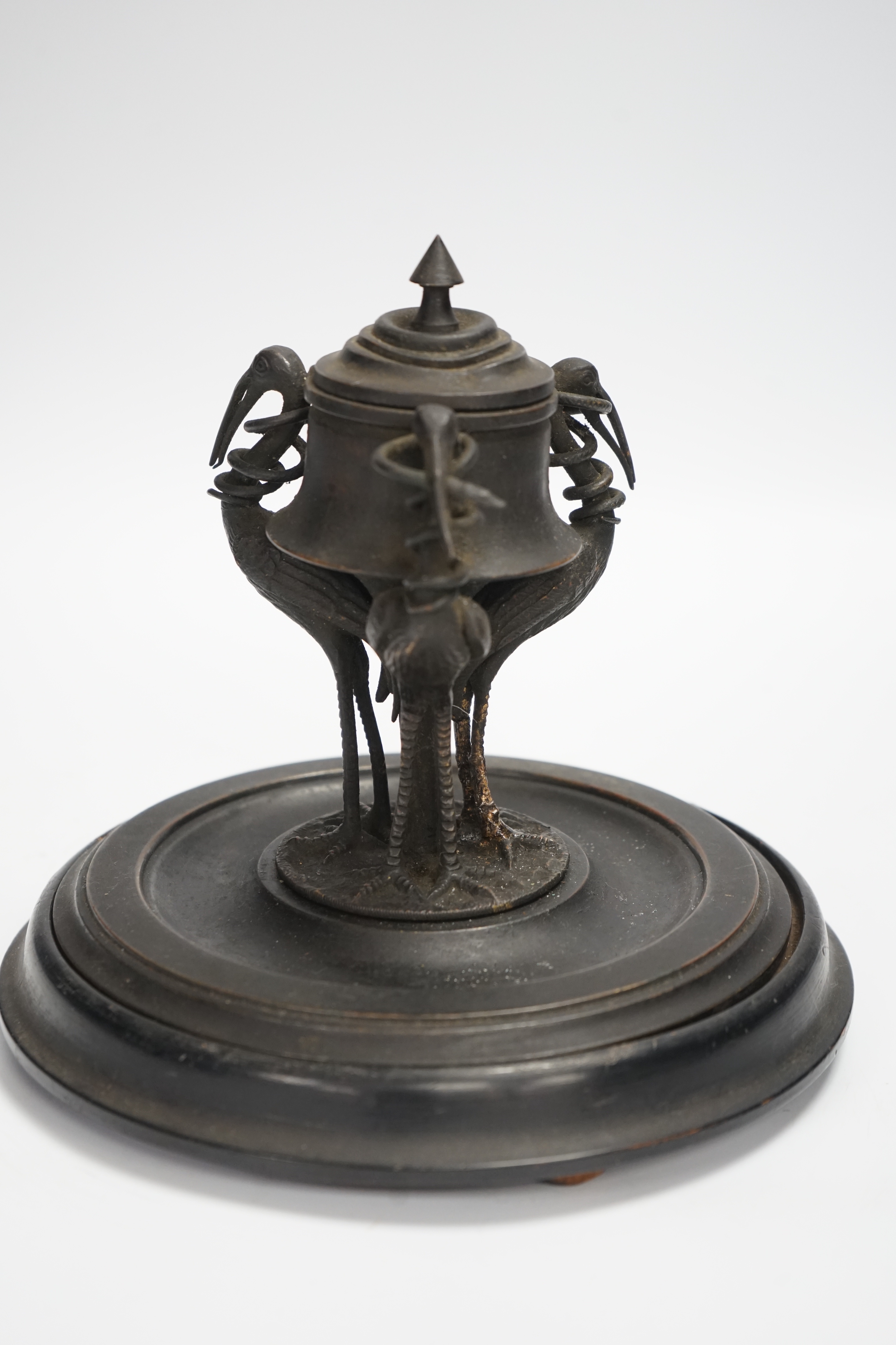 A late 19th century patinated metal inkwell, modelled with three cranes on an ebonised pine base, 18cm